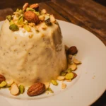 طبق بسبوسة بالزبادي نجلاء الشرشابي مزين باللوز والفستق على طاولة خشبية.